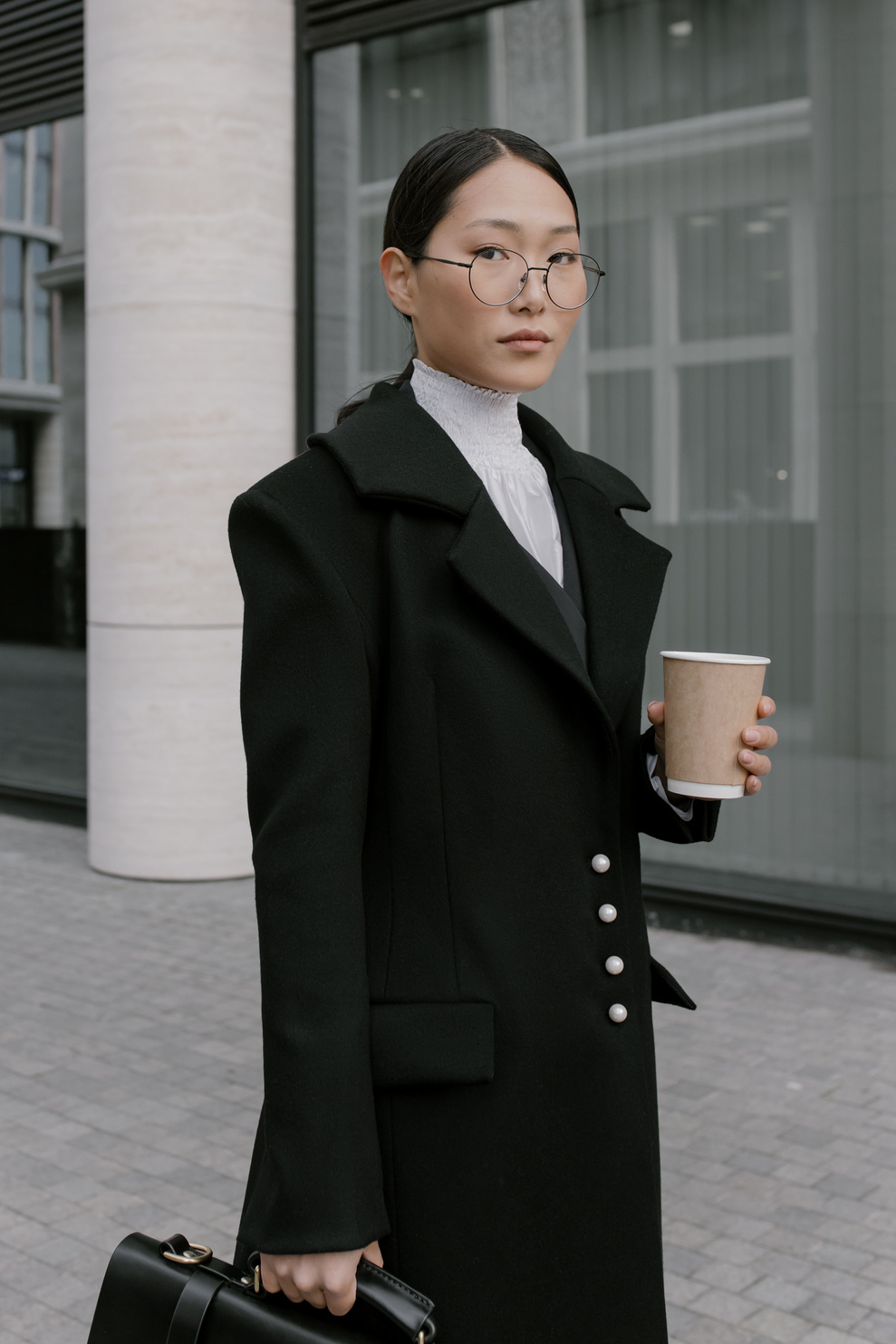 A Woman in Black Coat Wearing Eyeglasses while Holding a Cup of Coffee